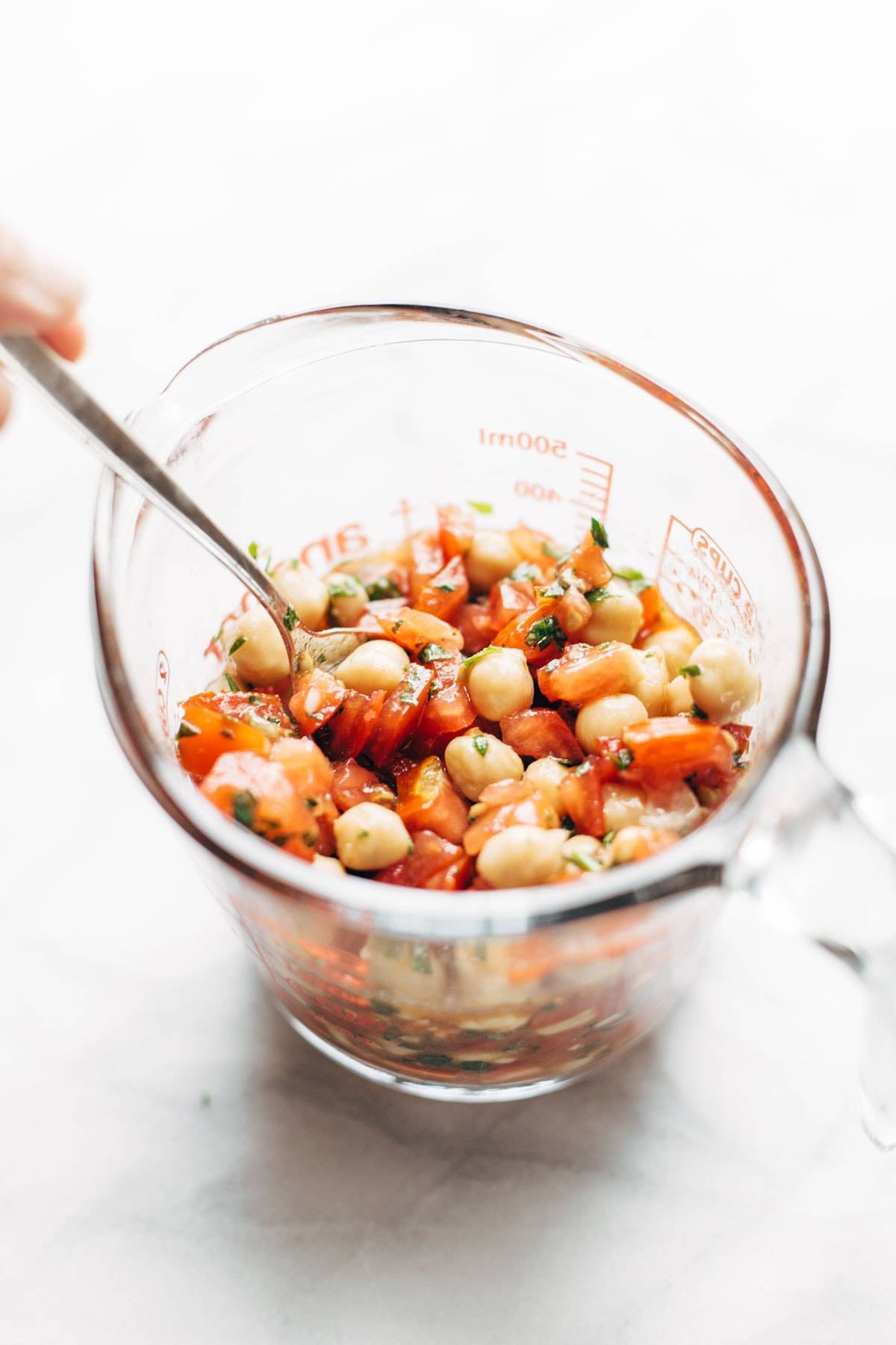 Marinated tomatoes and chickpeas in a measuring cup.