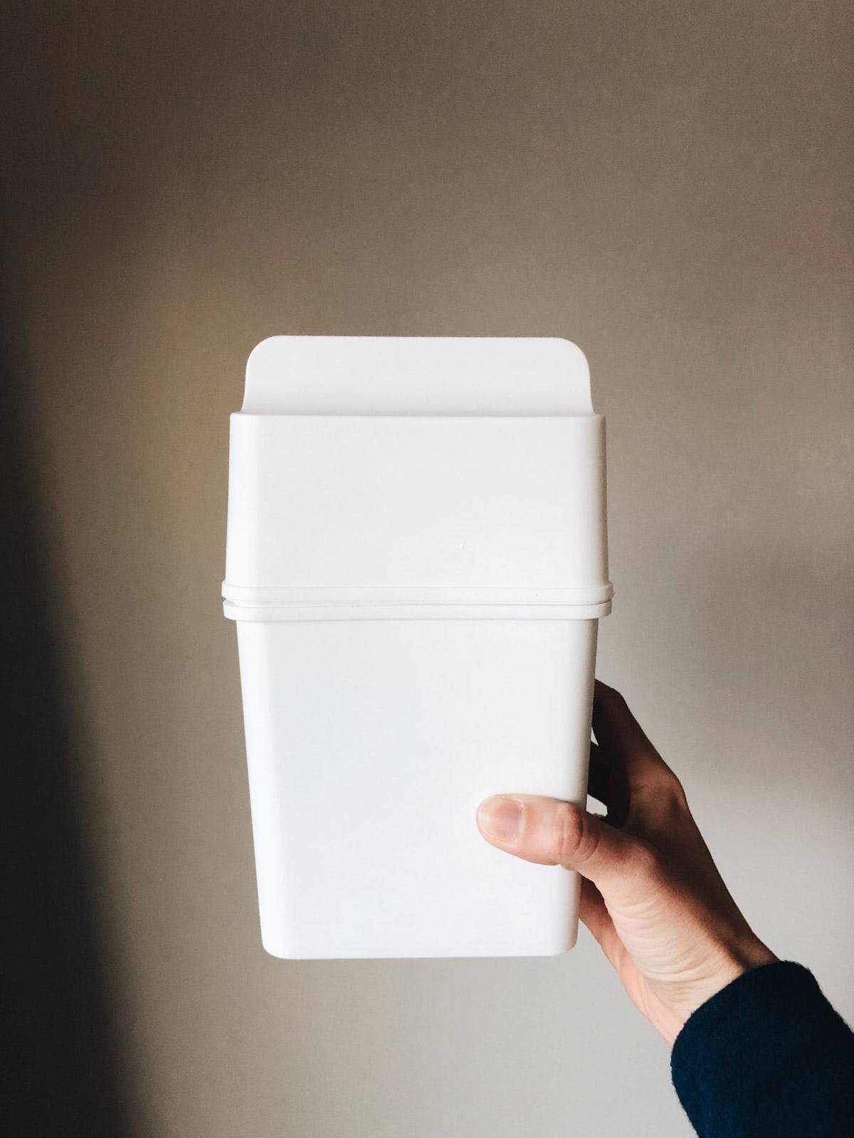A person holding up a white container in their right hand.