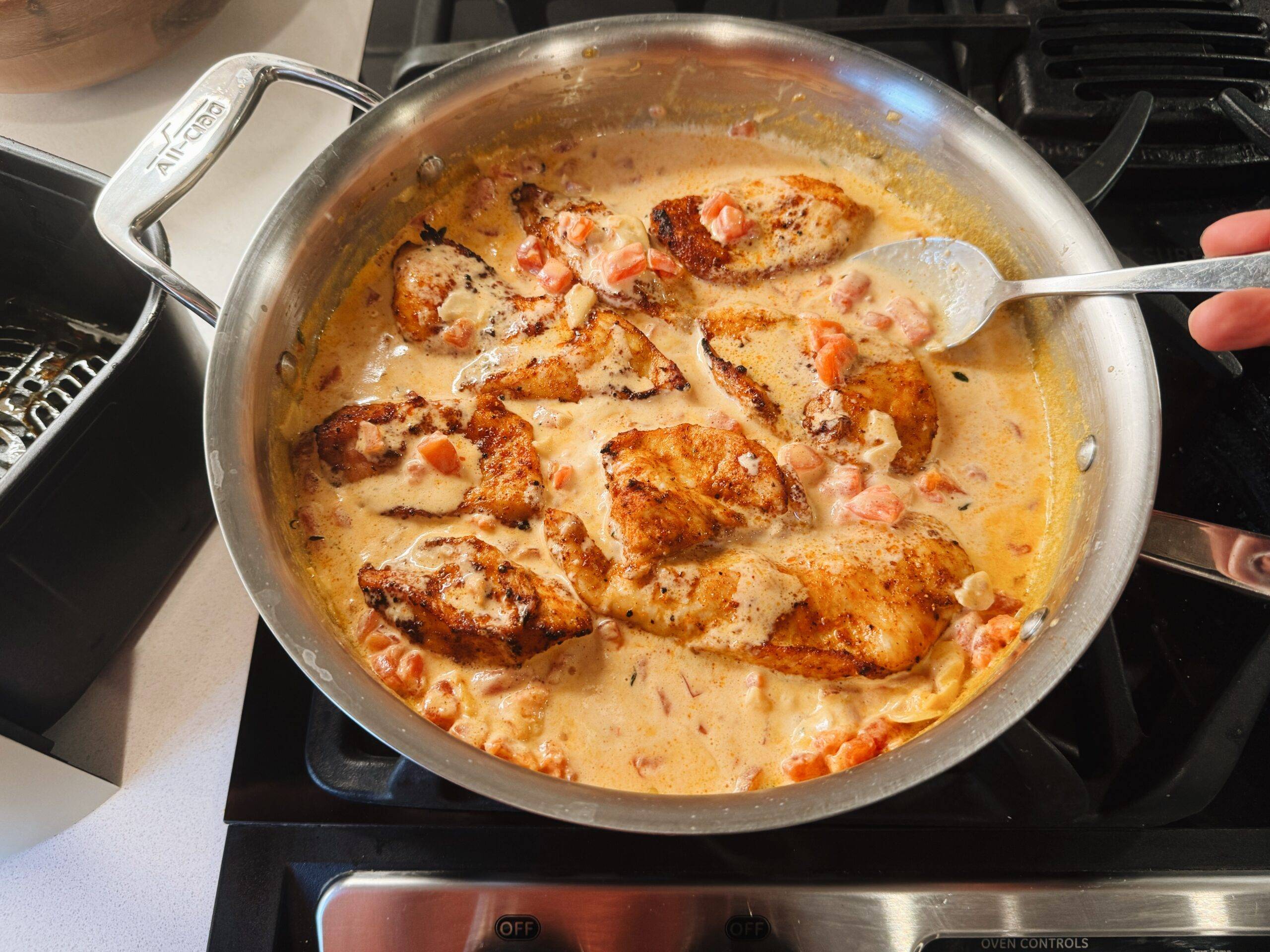 Spooning sauce over chicken in a pan.