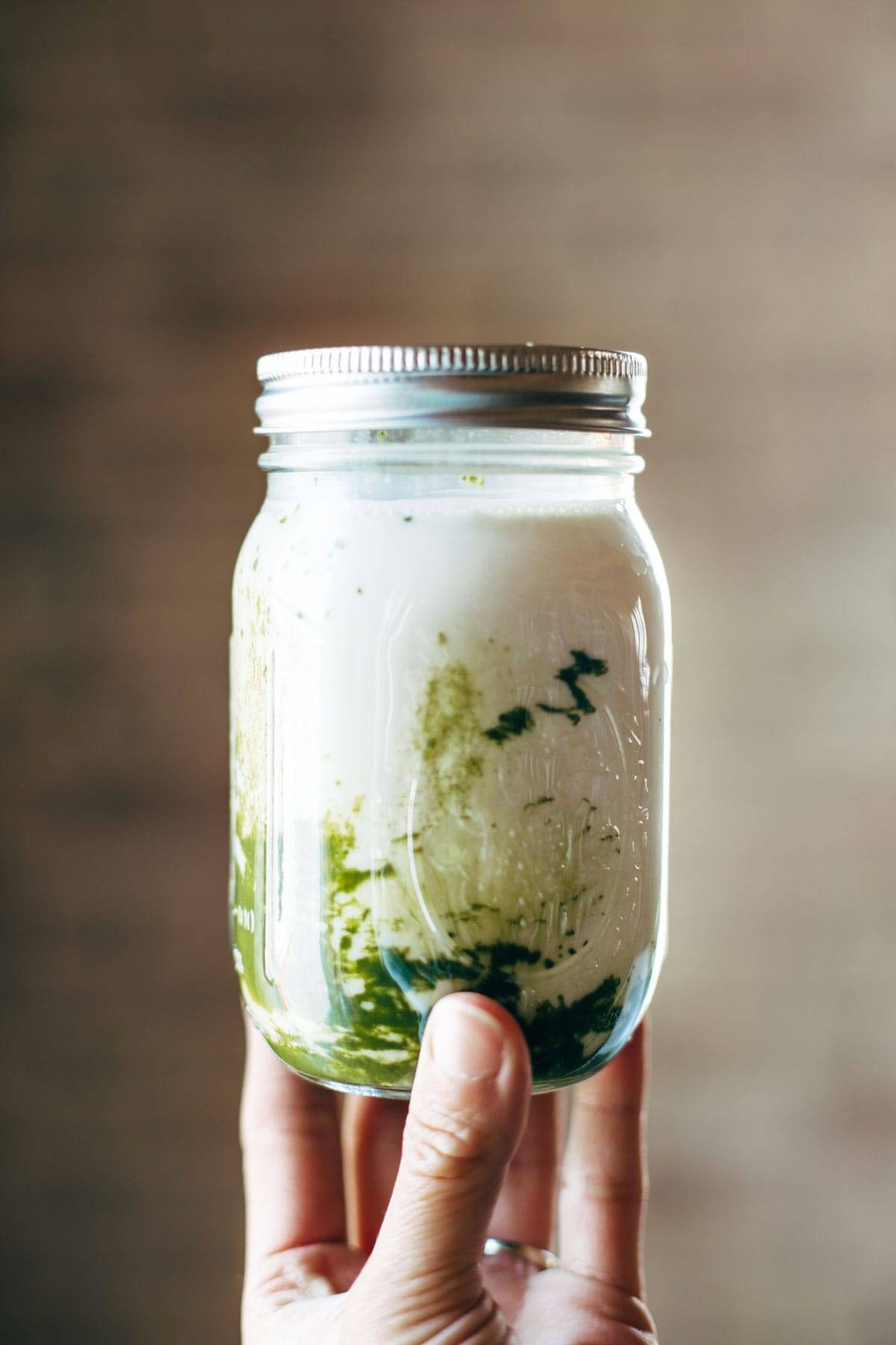 Iced Matcha Green Tea Latte in a jar with a white hand.
