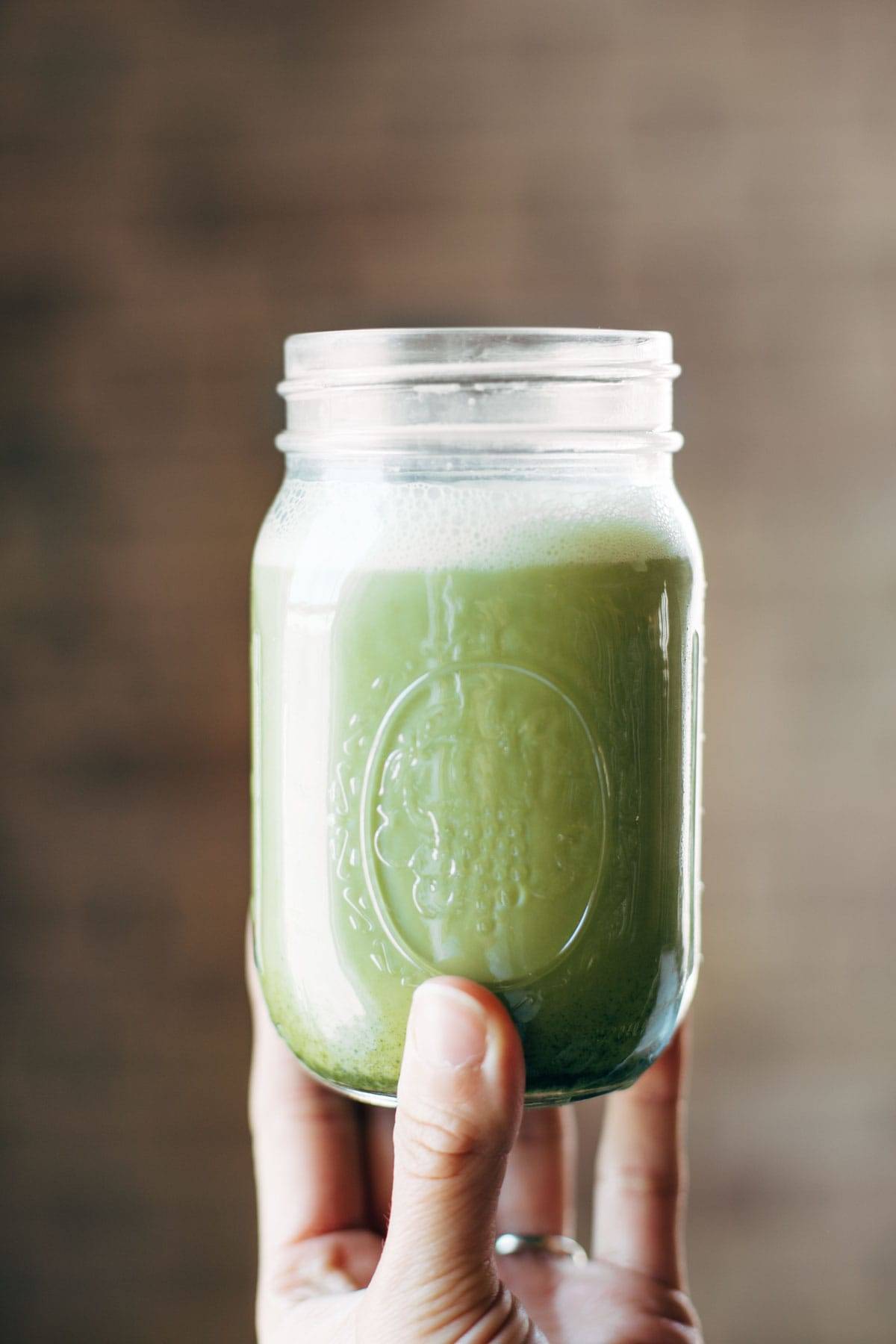Iced Matcha Green Tea Latte shaken in a jar with a white hand holding it up. 