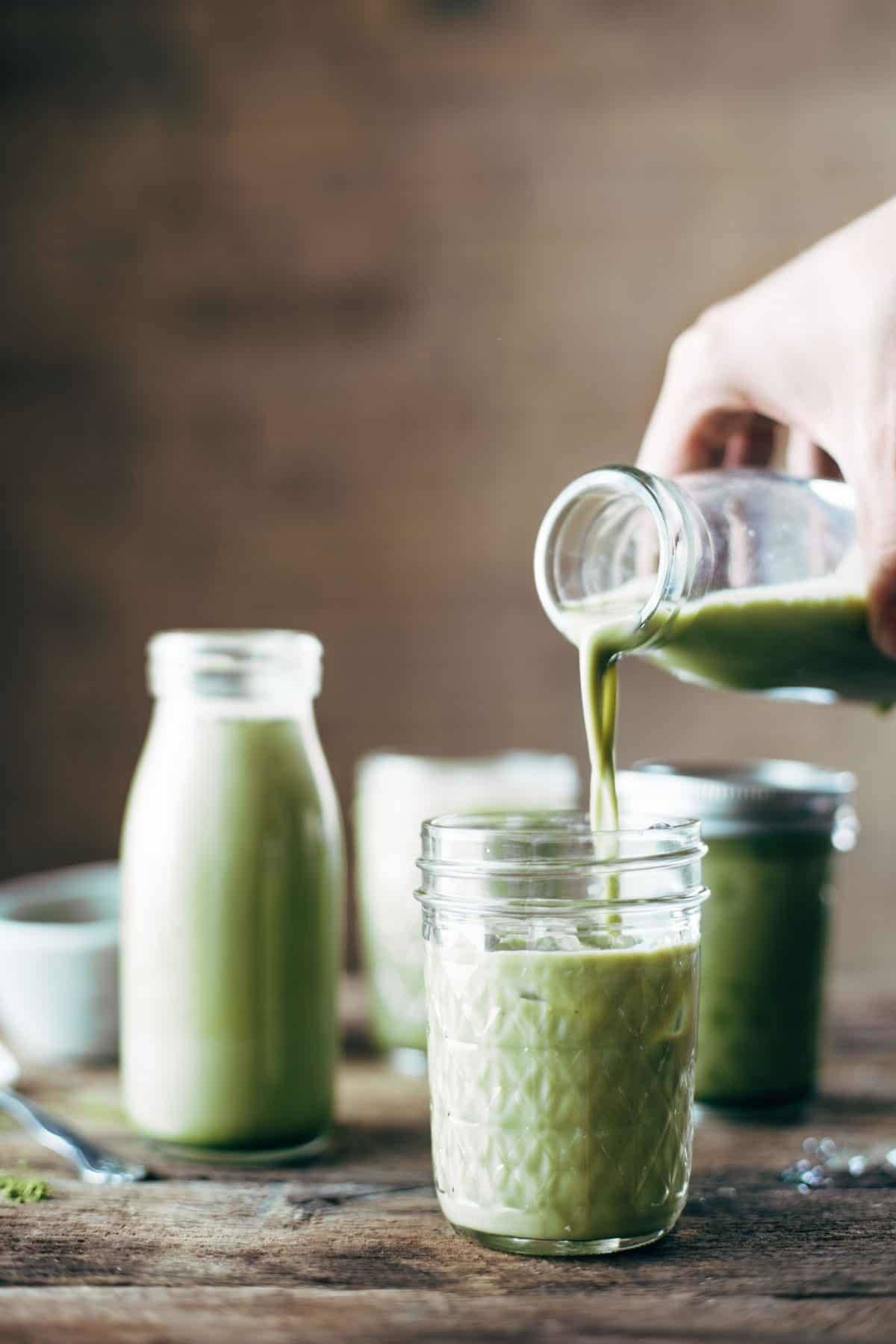 White hand pouring iced matcha green tea into a jar. 