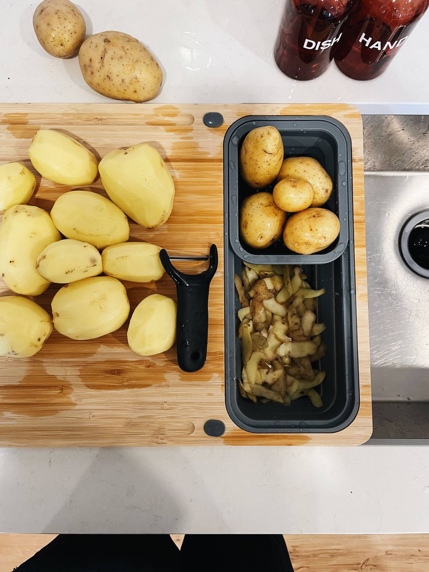 A cutting board with potatoes being peeled.