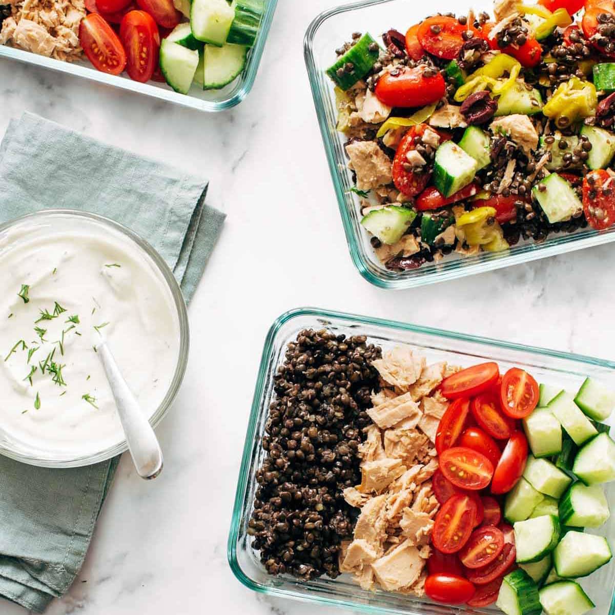 Greek salad meal prep in glass containers and a bowl of yogurt dip.