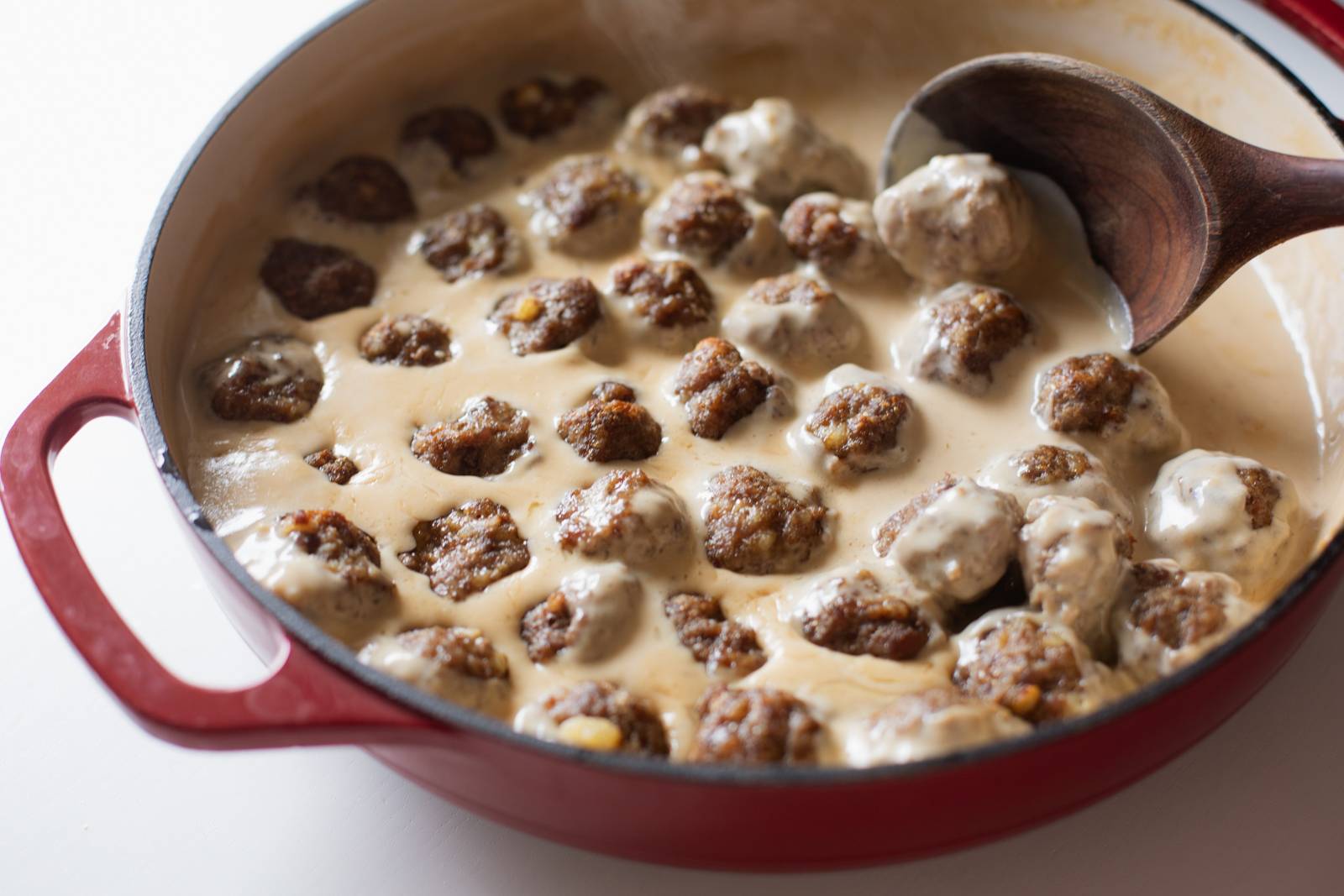 Mixing Swedish meatballs in a skillet with sauce.