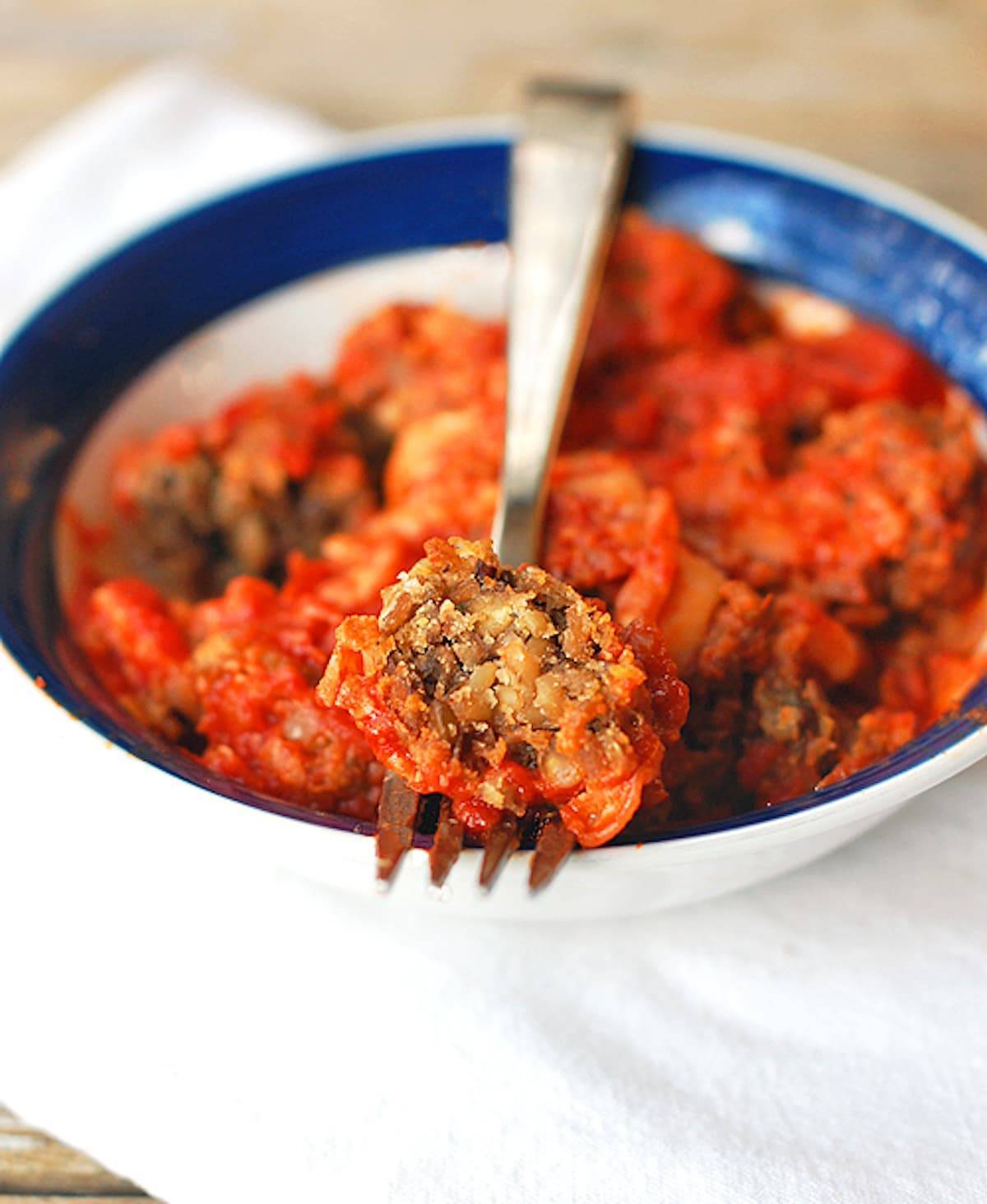 Meatless Meatballs with lentils and wild rice, and topped with marinara sauce and melted cheese on a fork.