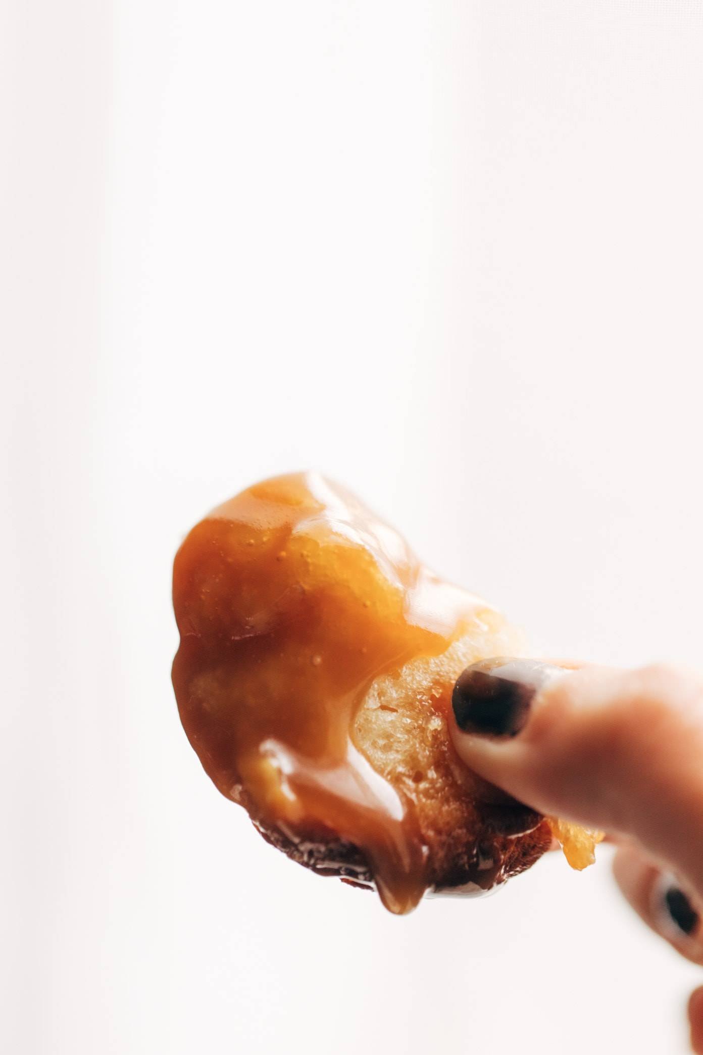 A woman holds a piece of monkey bread with caramel sauce dripping off of it.