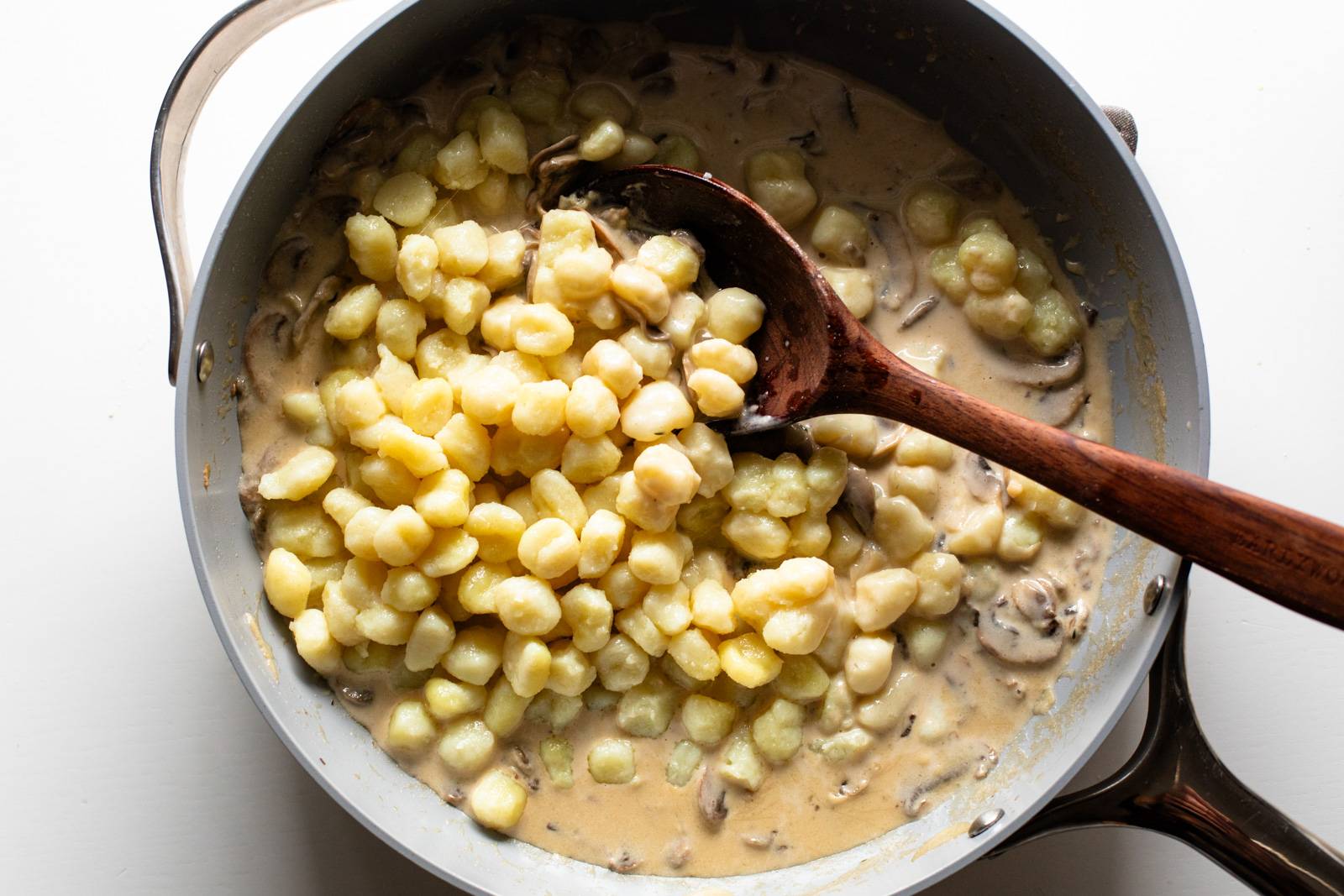 Stirring gnocchi into creamy mushroom sauce in a pan.