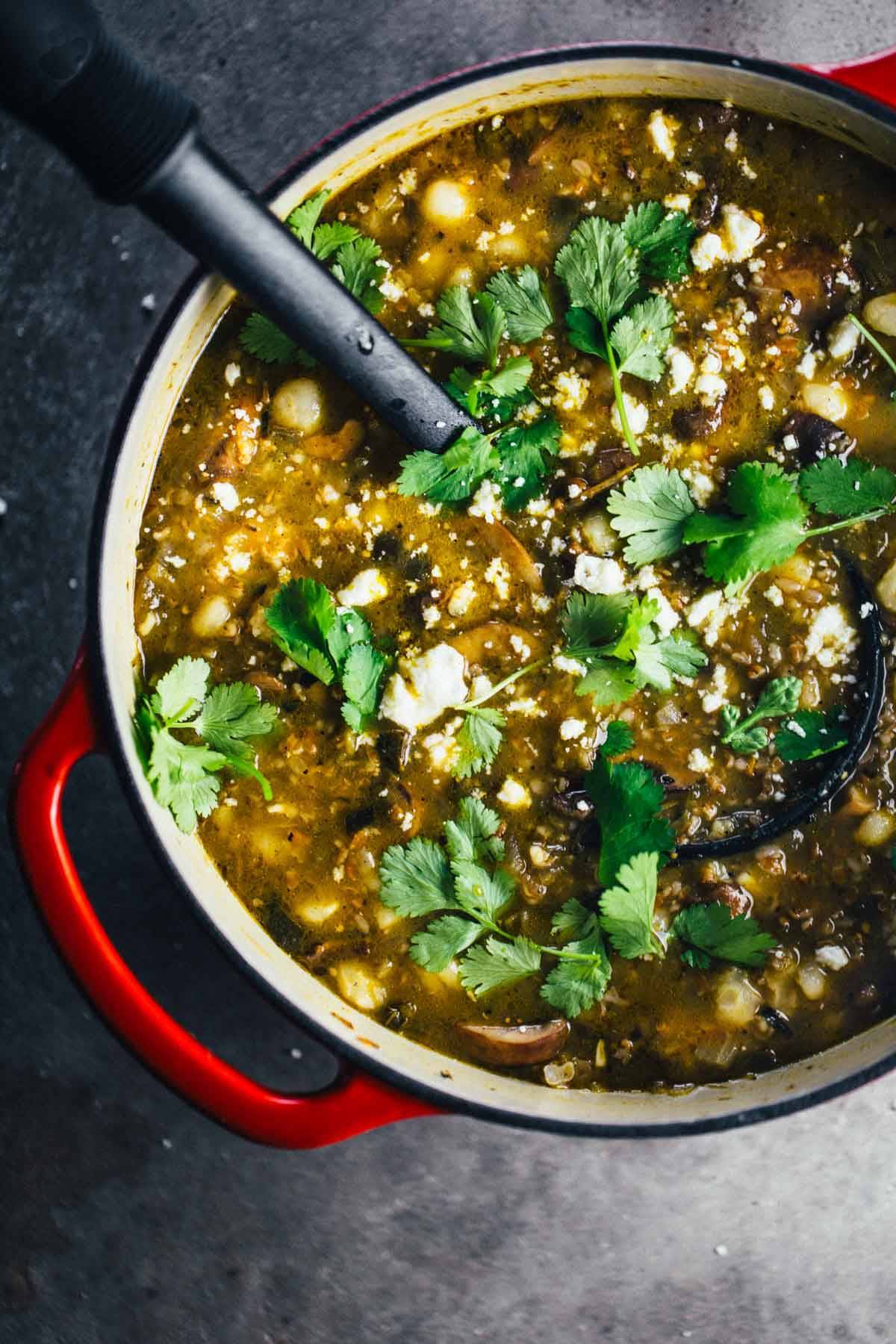 Mushroom Poblano Posole Verde in a dutch oven with a spoon and herbs.