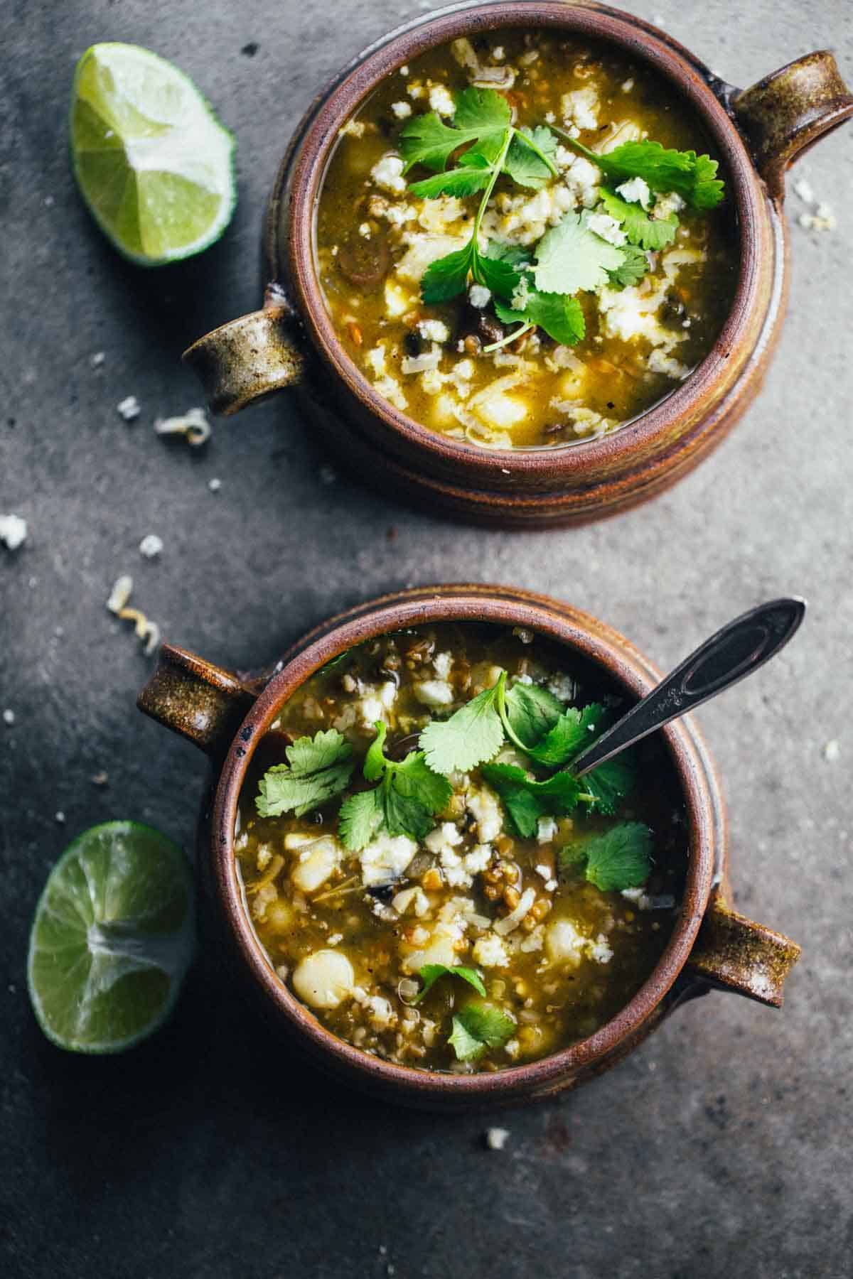 Mushroom Poblano Posole Verde in two bowls with limes.