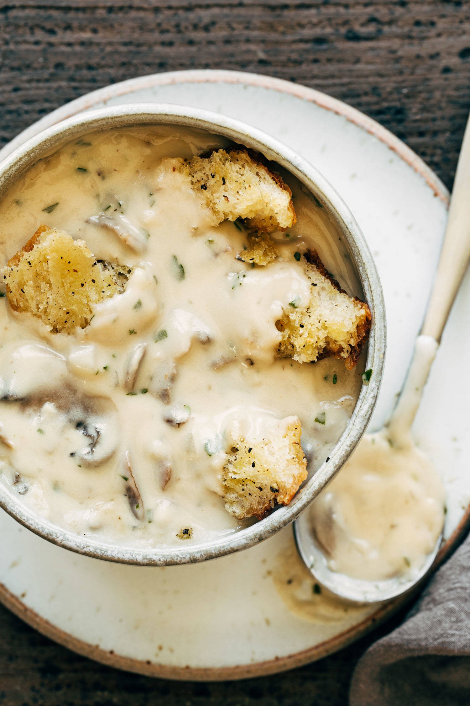 Creamy mushroom soup in a bowl. There's a spoon on the side and croutons on top of the soup.