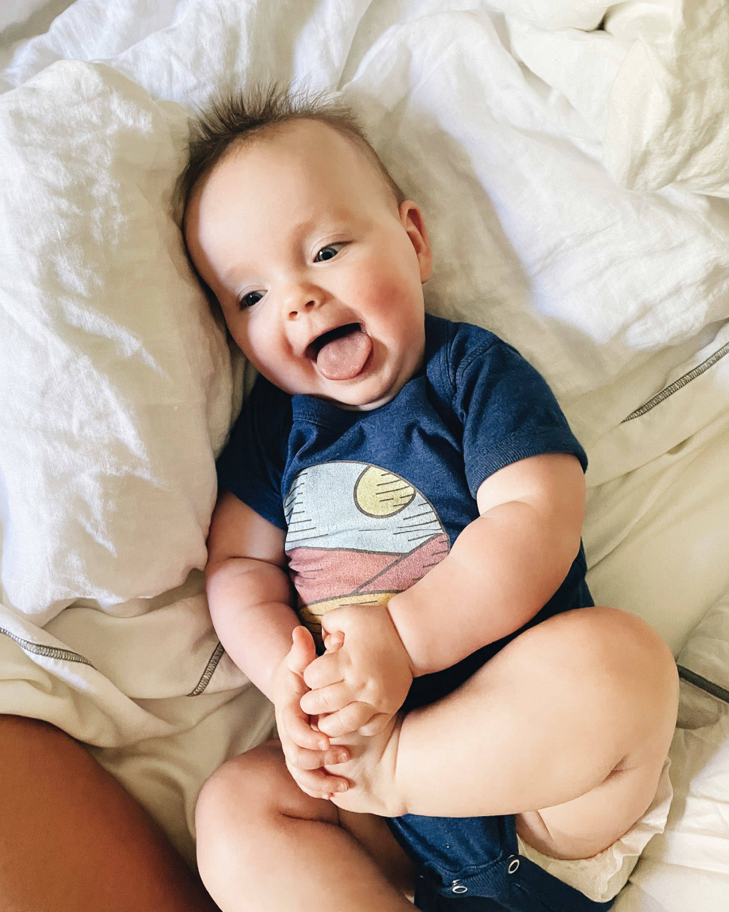 Happy baby with tongue out holding her feet. 