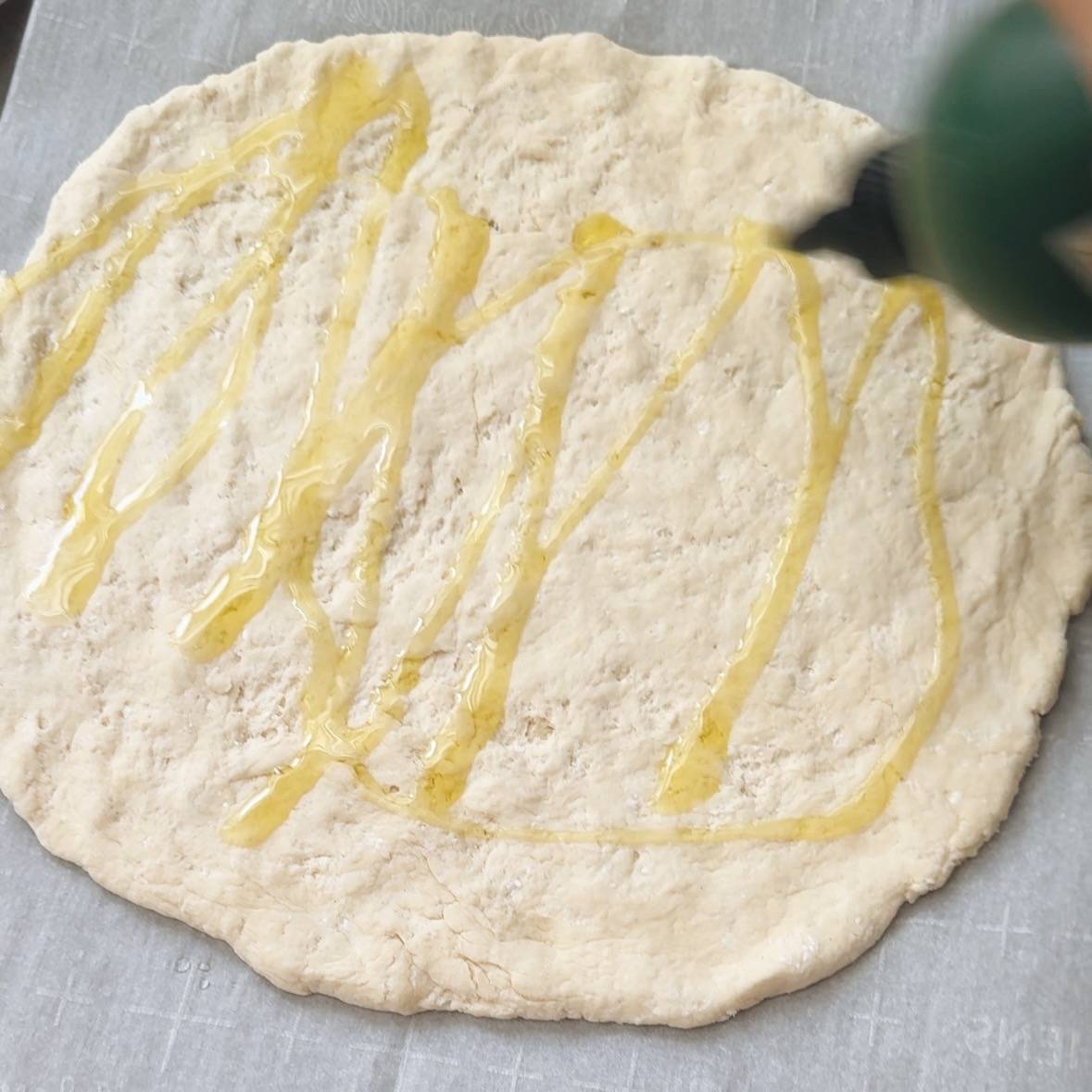 Drizzling olive oil on pizza crust before baking.