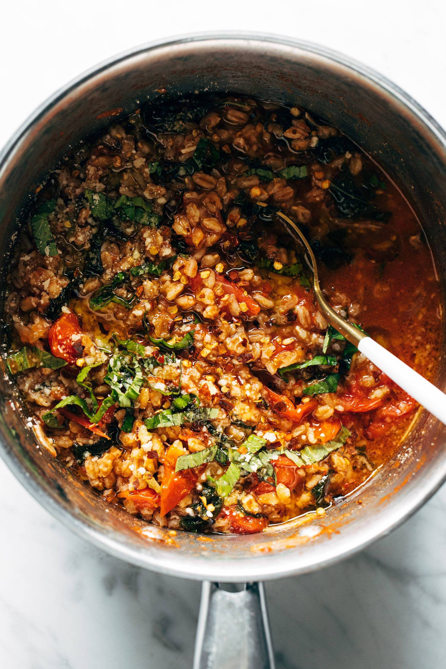 Overhead image of the farro, tomatoes, and kale in a pot with a gold spoon. 