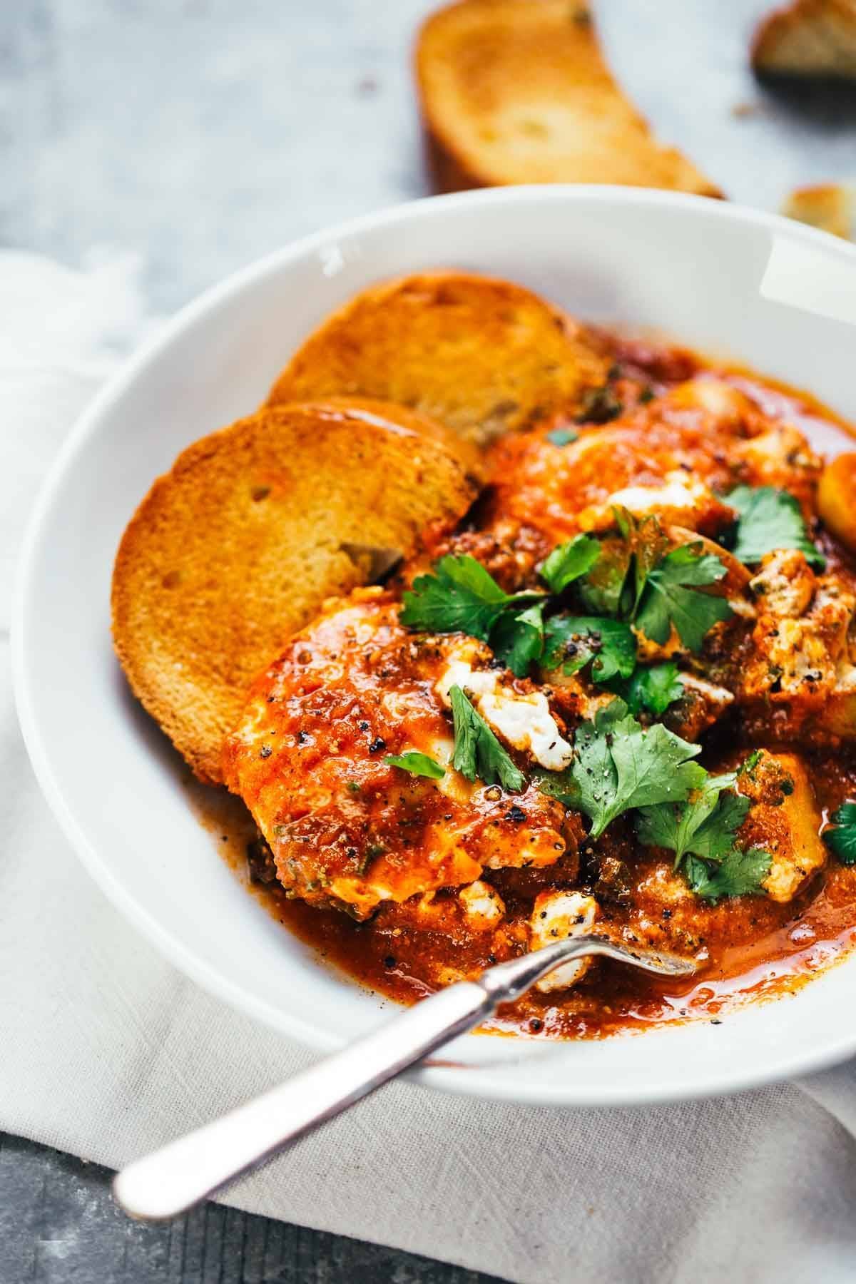 Spicy Eggs and Potatoes with a homemade tomato sauce, kale, potatoes, eggs, and creamy goat cheese on a white plate with a fork.