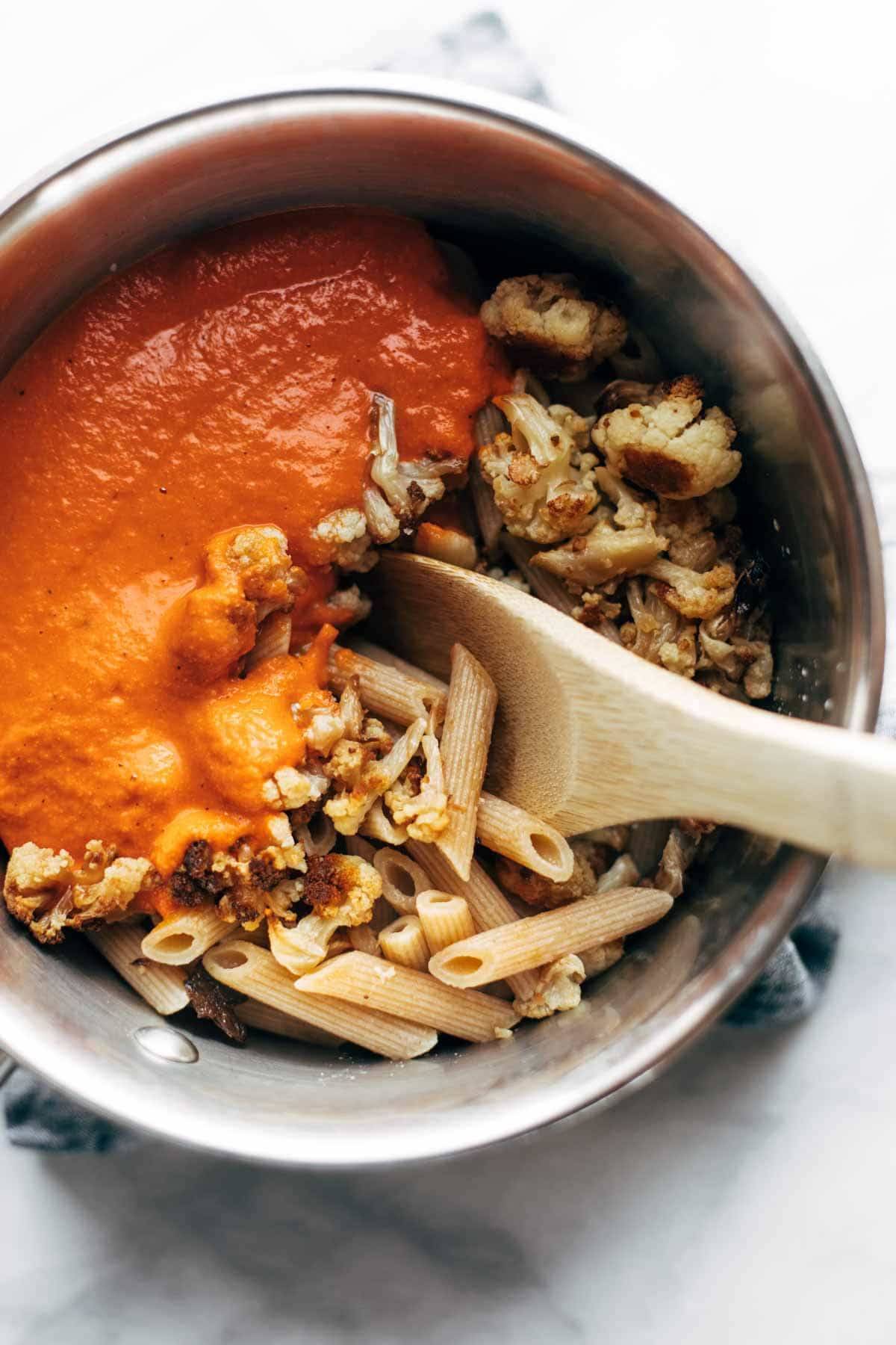 Mixing ingredients for Red Pepper Cashew Pasta in a mixing bowl with a wooden spoon.