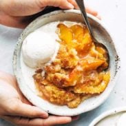 Peach cobbler in a bowl with ice cream.