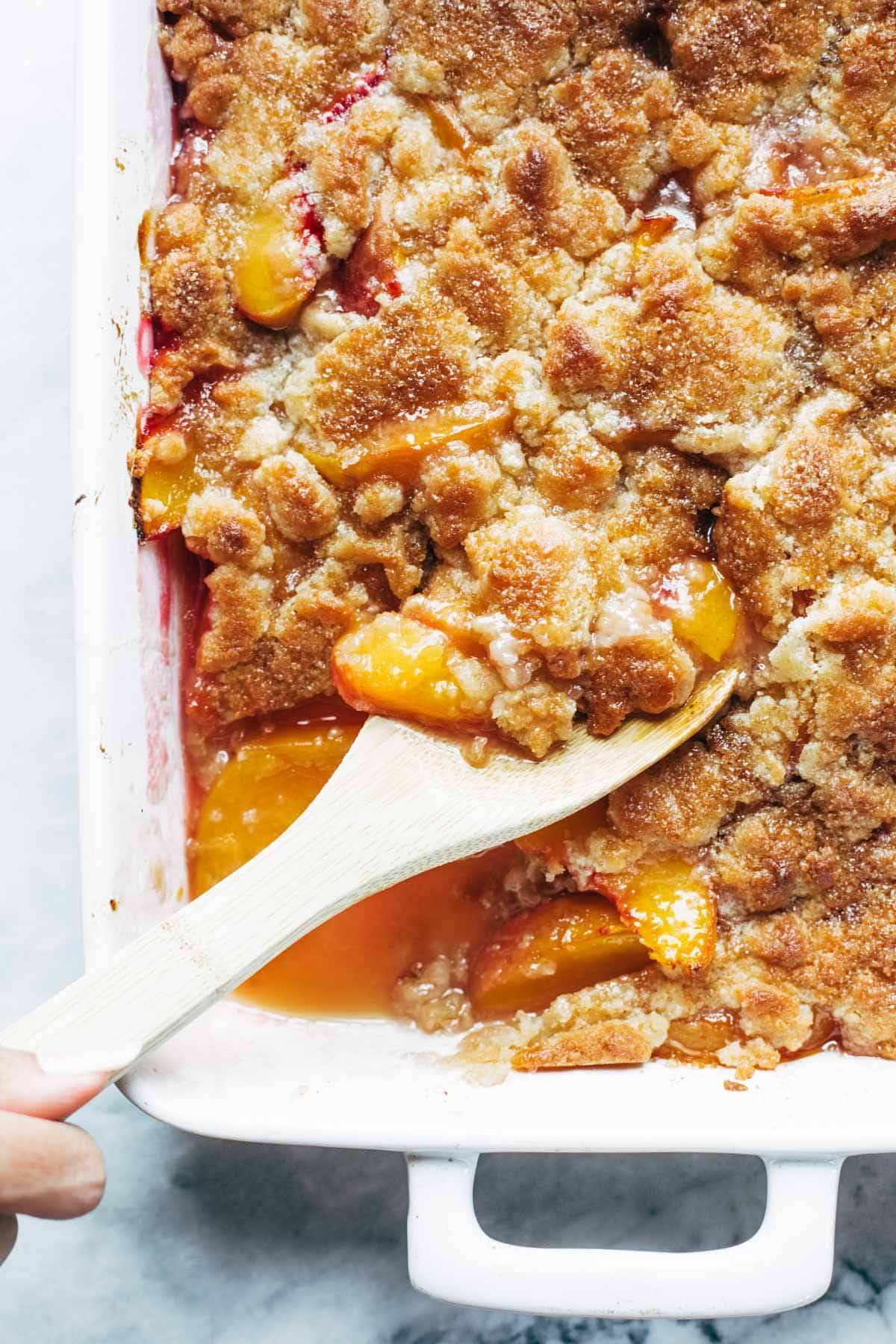 Peach cobbler in a pan with wooden spoon.