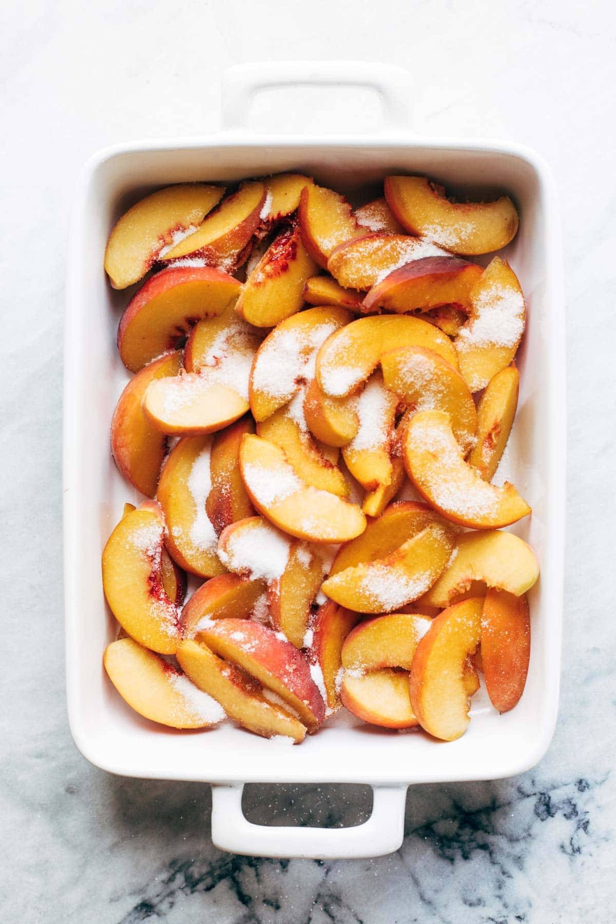 Peaches and sugar for peach cobbler in a pan.