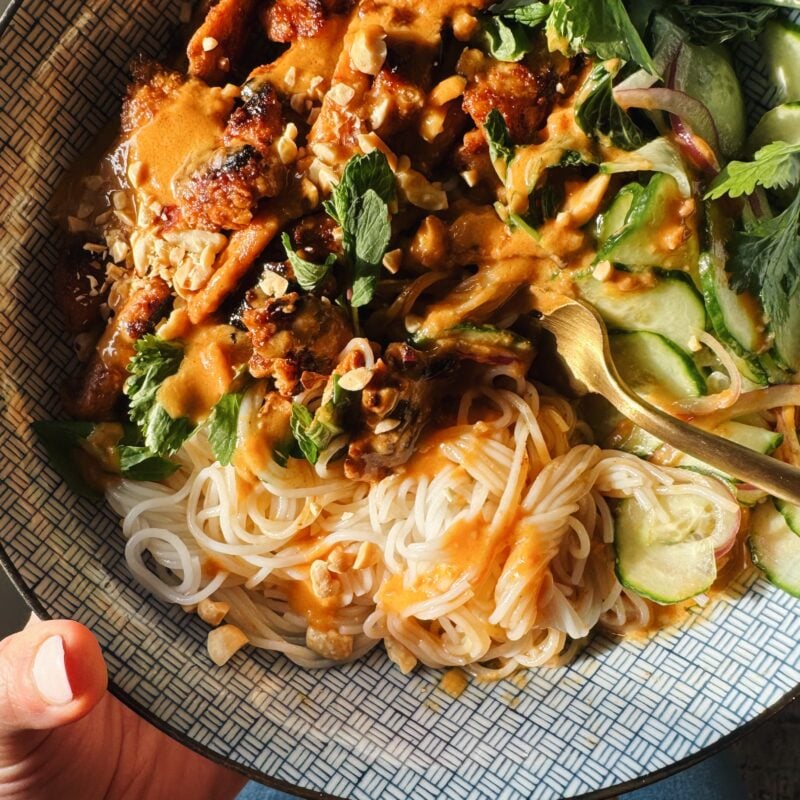 Peanut chicken in a bowl with noodles and herbs.