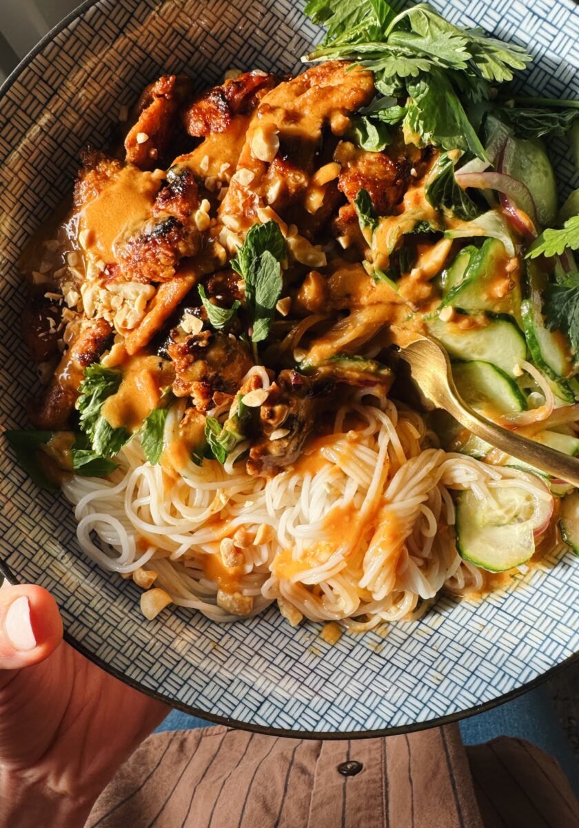 Peanut chicken in a bowl with noodles and herbs.