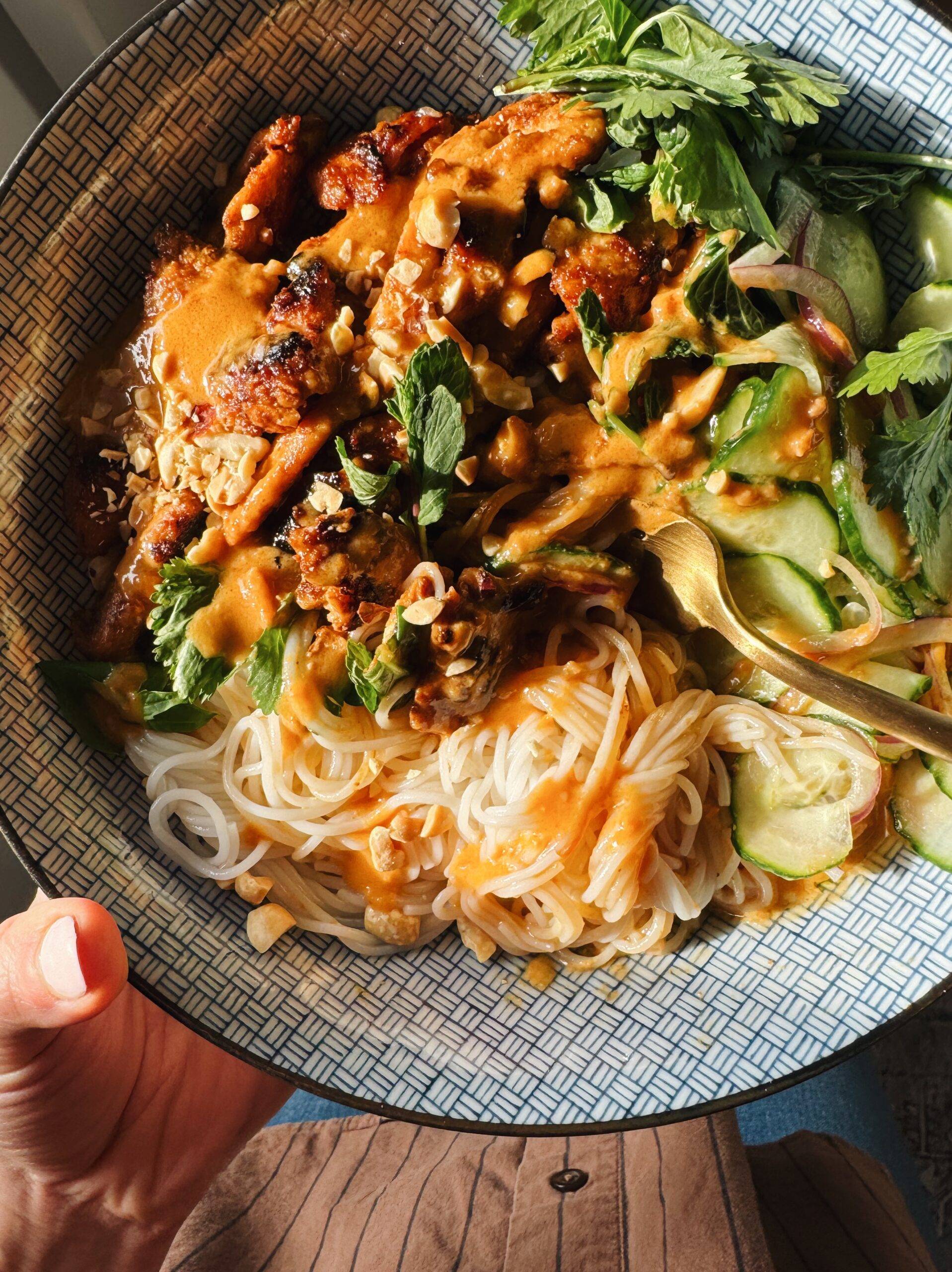 Peanut chicken in a bowl with vermicelli noodles and cucumber salad.