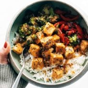 Sauced broccoli, tofu, and peppers sit on a bed of rice in a bowl with a fork.