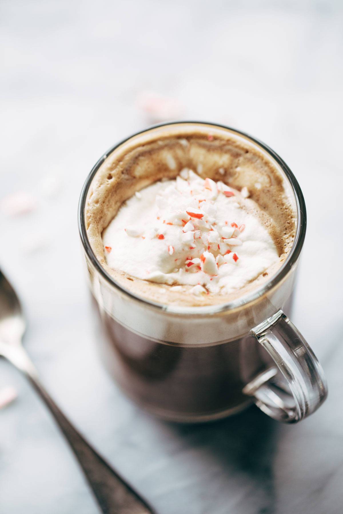 Clear coffee cup filled with peppermint mocha, topped with whipped cream and candy canes.