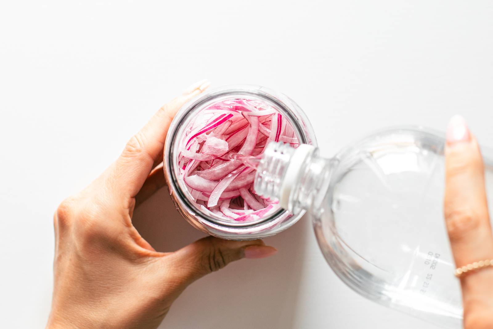 White vinegar being poured into a jar of red onions.