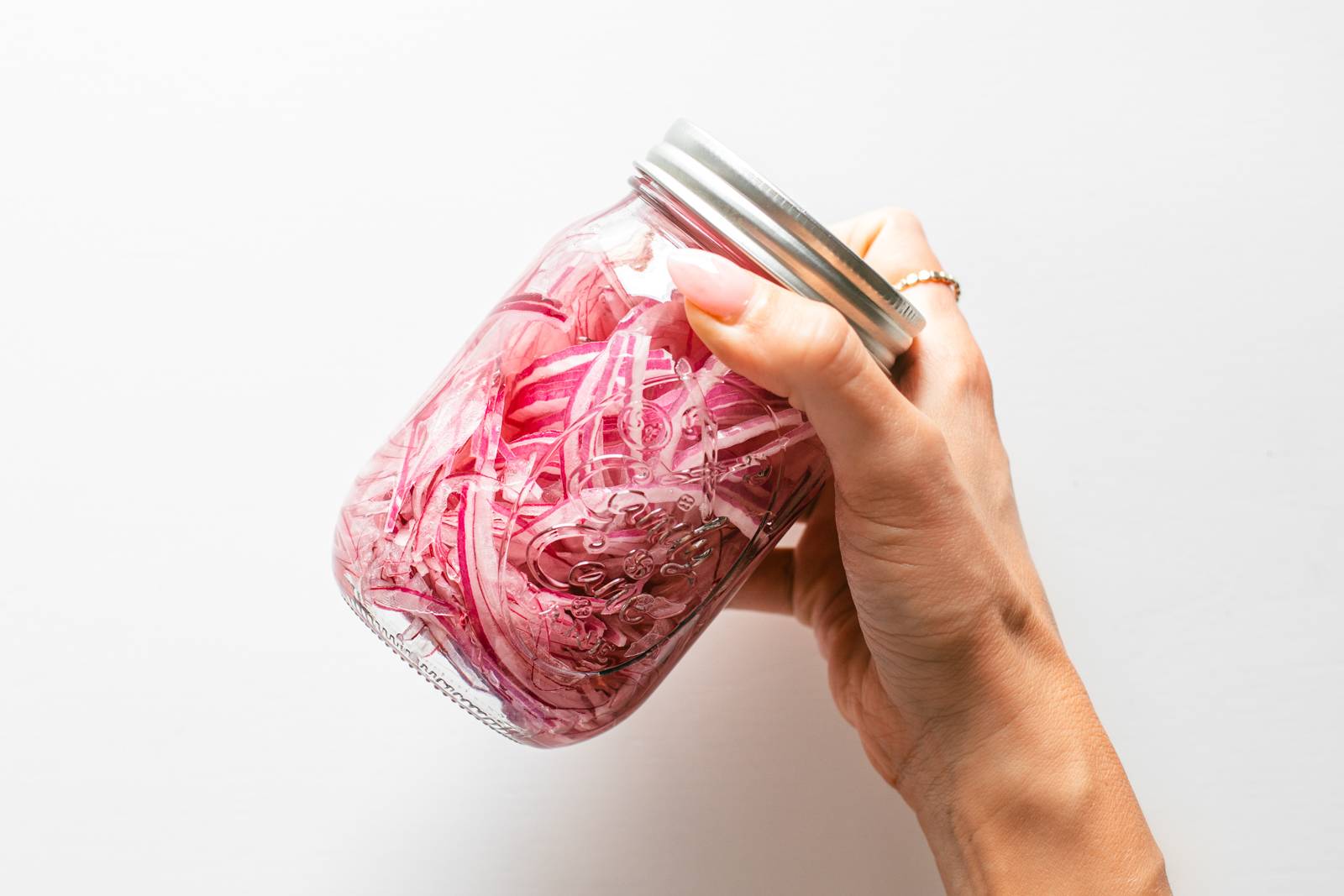 A white hand holds a jar of red onions.