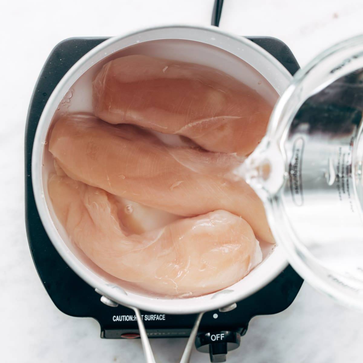 Boiling chicken breasts in water.