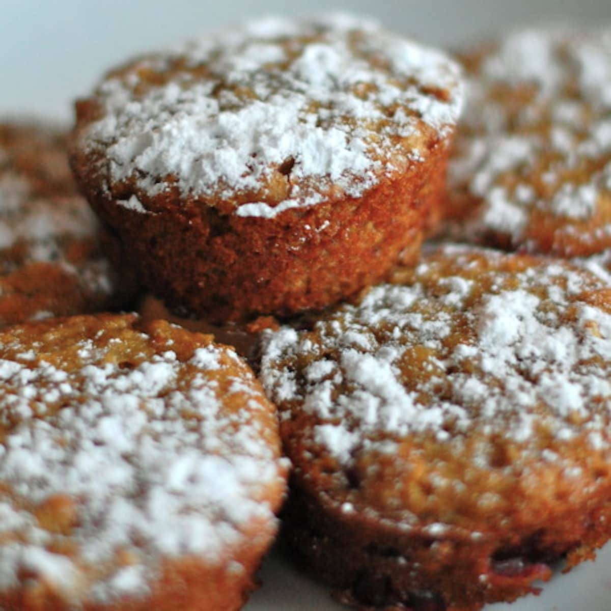 A stack of pomegranate orange muffins with powdered sugar topping.