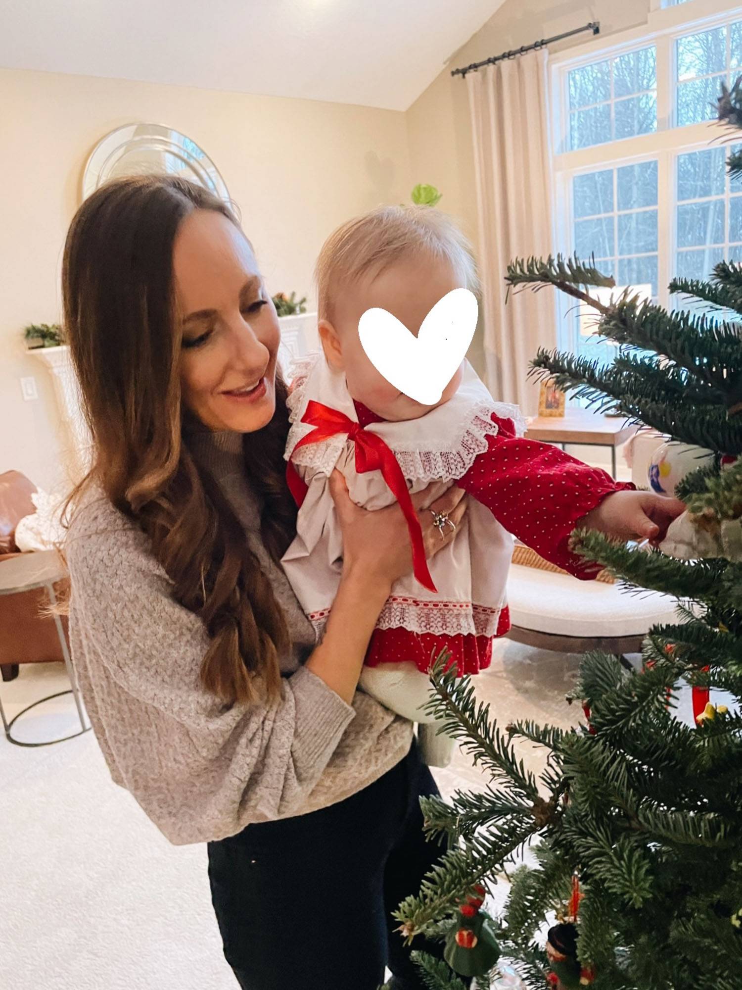Woman and baby dressed in formal clothing playing with Christmas ornaments on a tree.