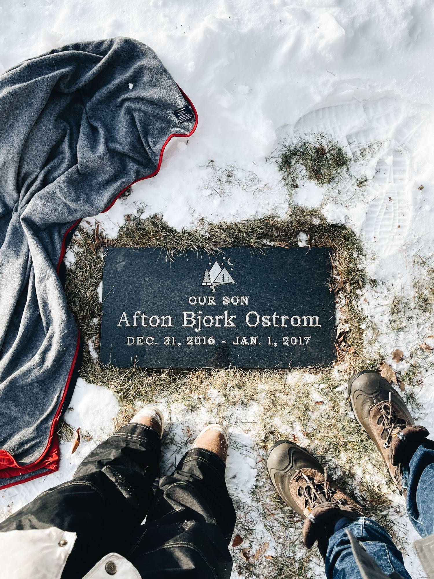 Two pairs of feet next to a grave surrounded by snow.
