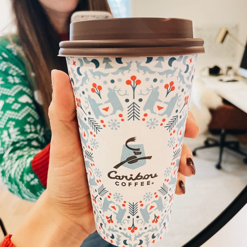 White woman holding holiday themed coffee cup.