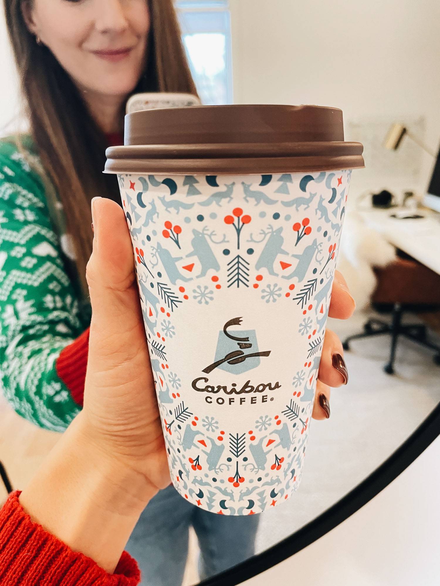 White woman holding holiday themed coffee cup.