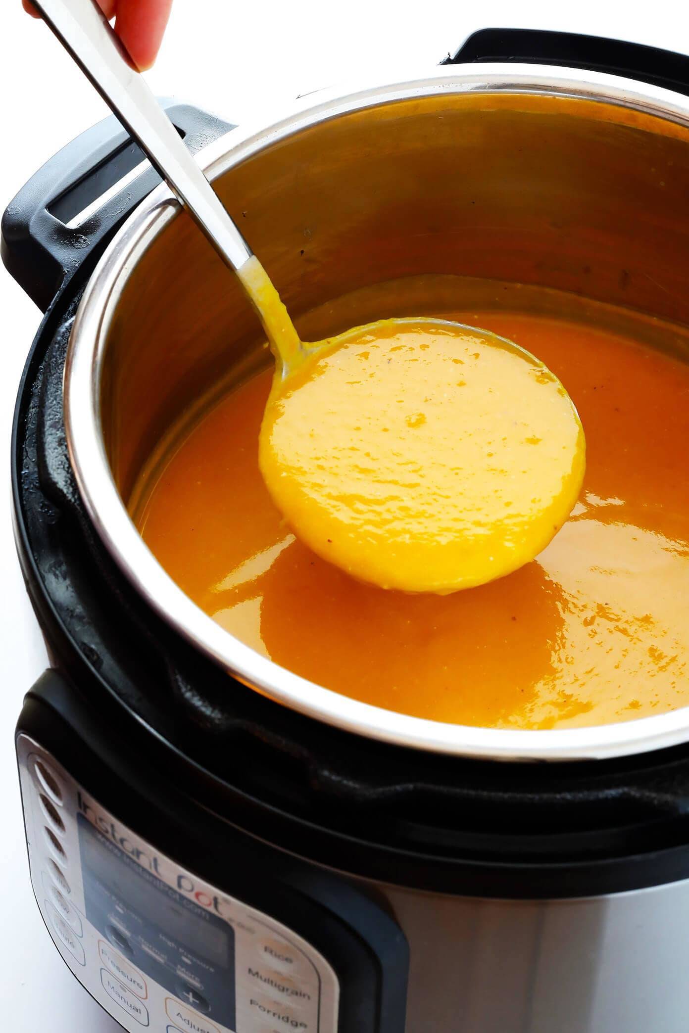A large pot filled with Butternut Squash Soup and a scoop holding filled with it.
