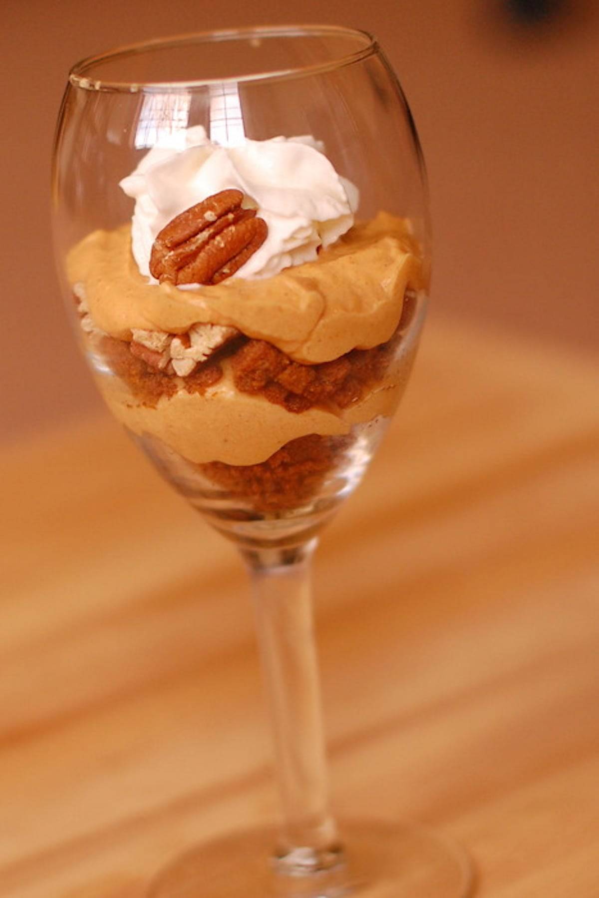Pumpkin pecan cheesecake parfait in a glass topped with whipped cream and a pecan.