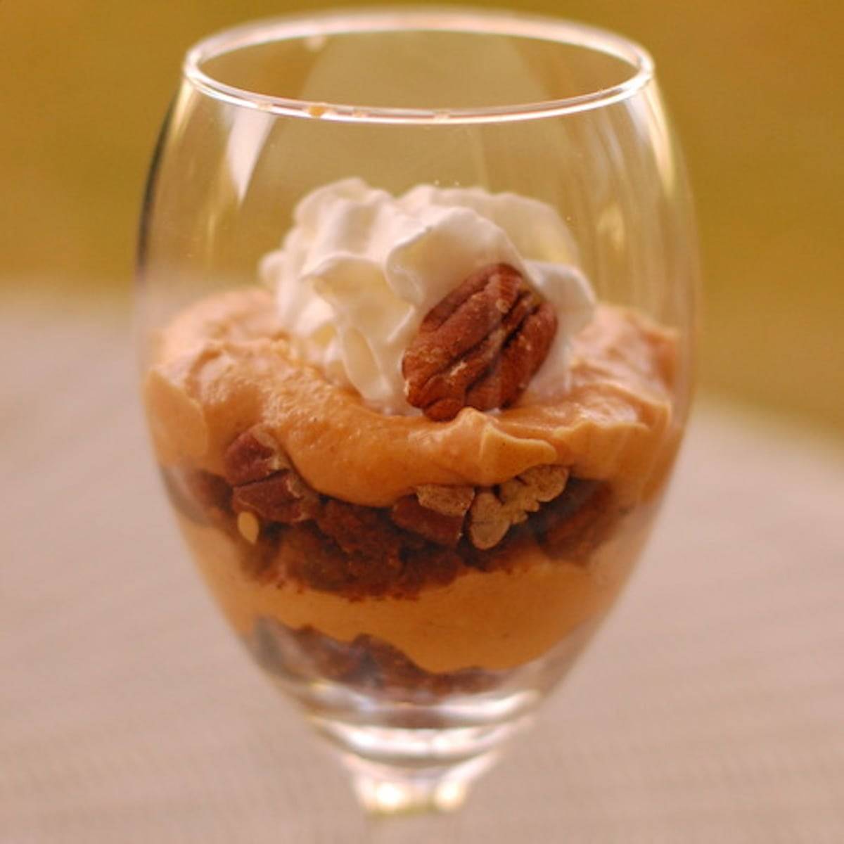 Pumpkin pecan cheesecake parfait in a glass with whipped cream and a pecan.