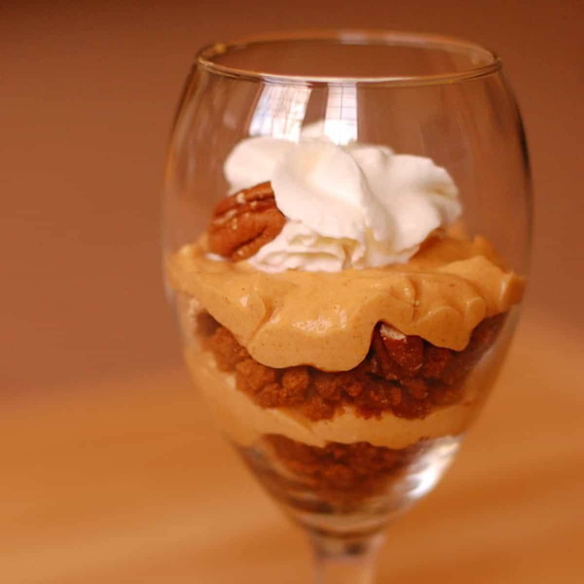 Pumpkin pecan cheesecake parfait in a glass topped with whipped cream.