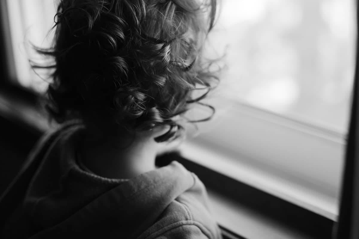 A black and white photo of a child looking out the window.