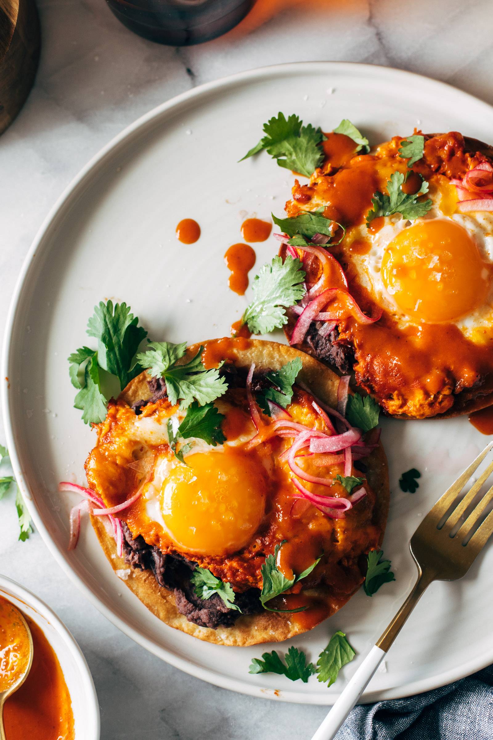 Red chile tostadas on a plate with eggs and a gold fork.