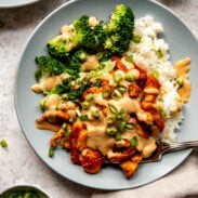 Red curry chicken stir fry on a plate with cashew sauce, broccoli, and rice