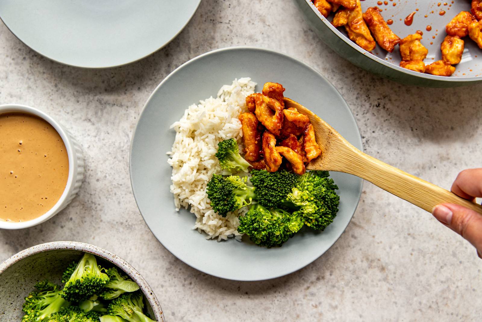 Red chicken curry is added to a plate with broccoli and cooked rice