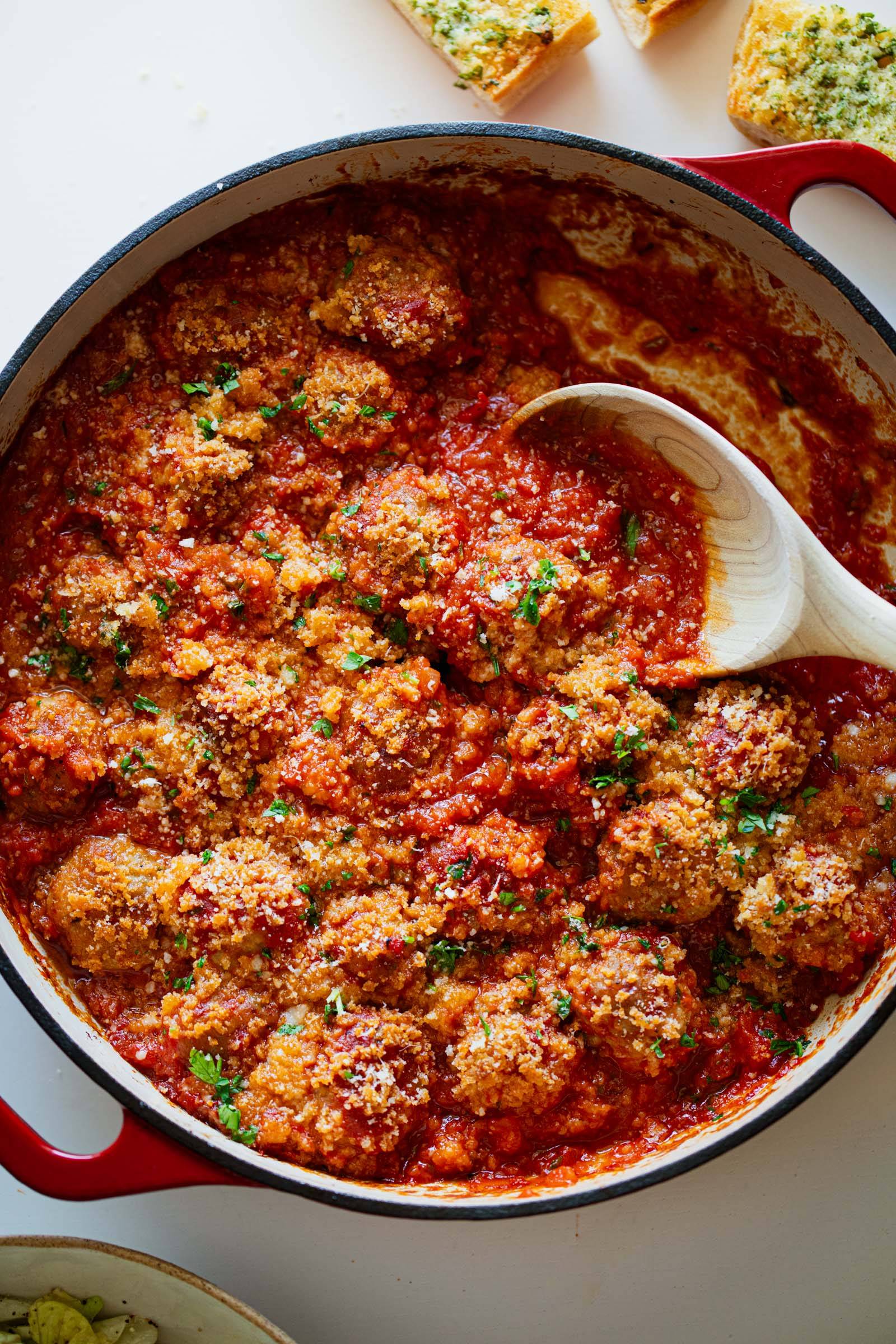 Meatballs in a skillet with red sauce and breadcrumbs.