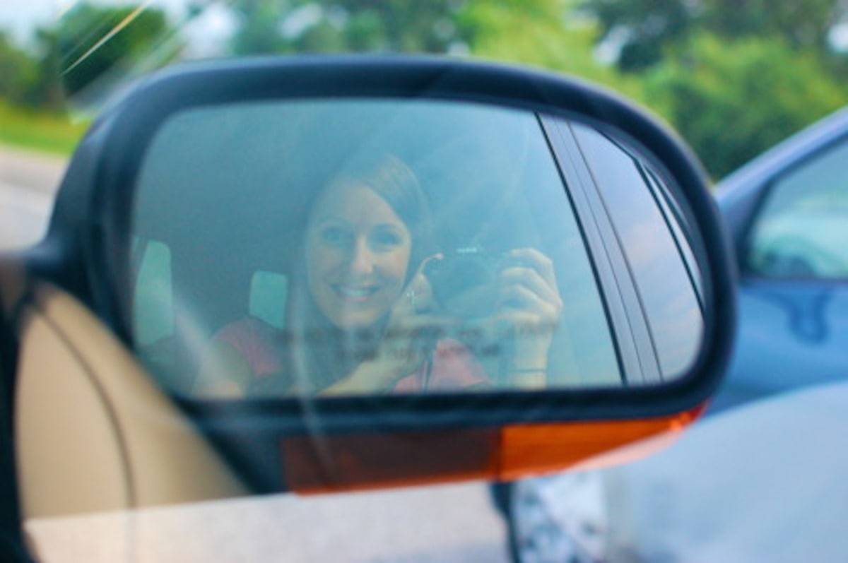 Woman taking a photo of herself through a car mirror.