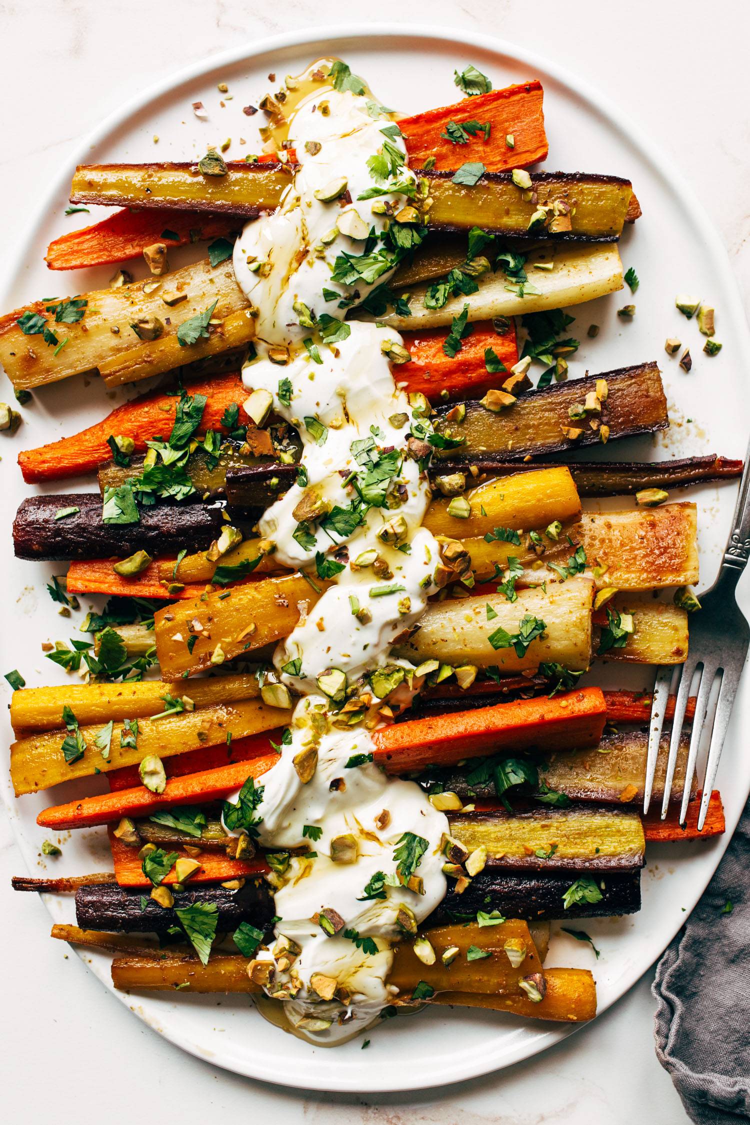 Roasted carrots on a plate with yogurt sauce, honey, toppings, and a fork.