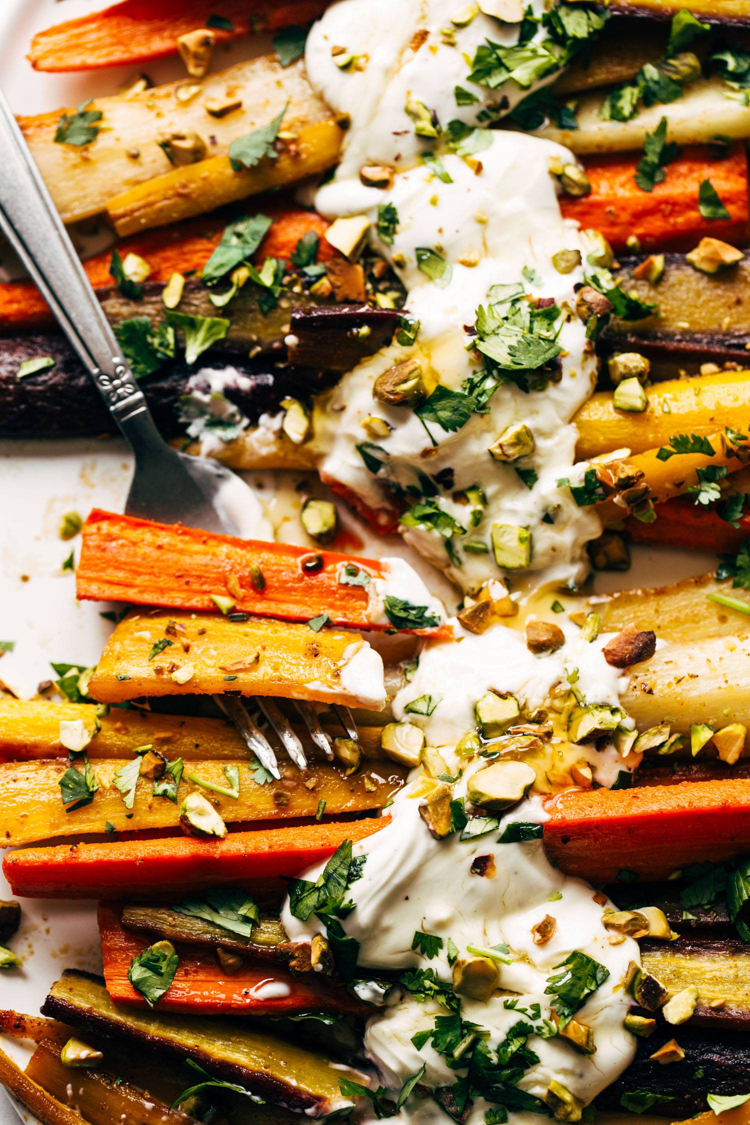 Heirloom carrots on a sheet pan with yogurt sauce and a fork.