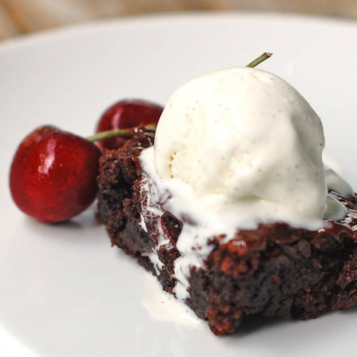 Roasted cherry brownie with ice cream and cherries on a white plate.