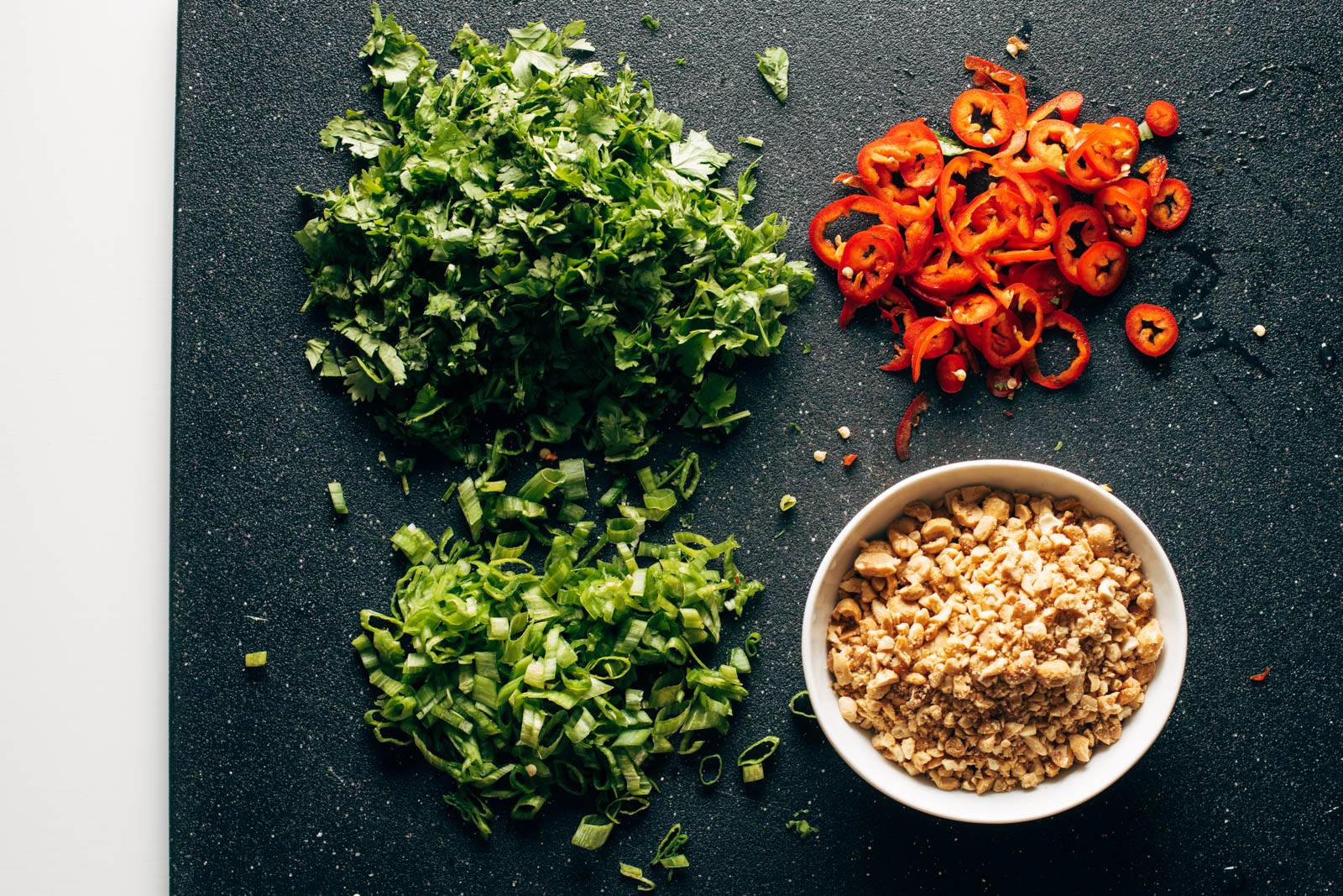 Chopped herbs, peppers, and peanuts on a cutting board